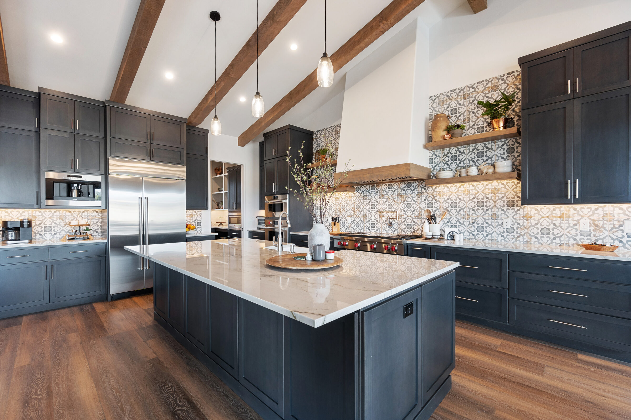 Contemporary kitchen with dark custom-style cabinetry, a large marble island and exposed wood ceiling beams